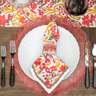 Dining table setting with floral napkin, white plate, and cutlery on a colorful tablecloth.