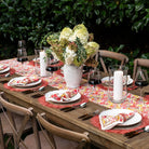 Dining table set for a meal with floral centerpiece, wine glasses, and cutlery outdoors.