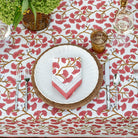 A table setting featuring a folded cotton napkin with a ginkgo leaf pattern in coral hues, displayed on a matching tablecloth
