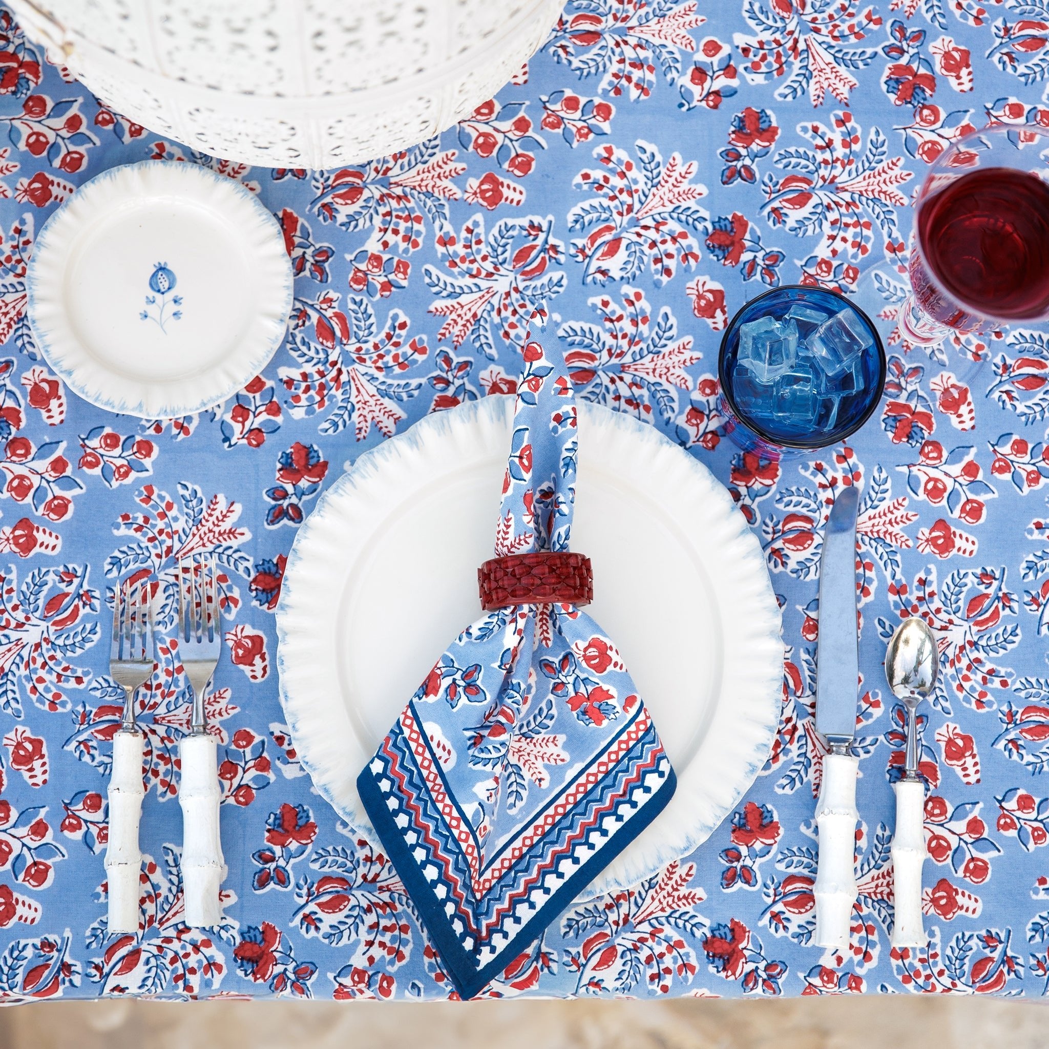 Table setting with floral tablecloth, plates, cutlery, and napkin on a wooden table.