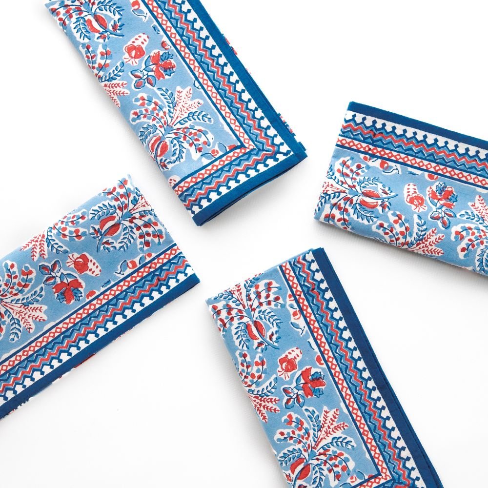 Set of four blue napkins with red and white floral patterns on a white background