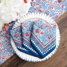Set of blue floral patterned napkins on a white plate with a wooden table.