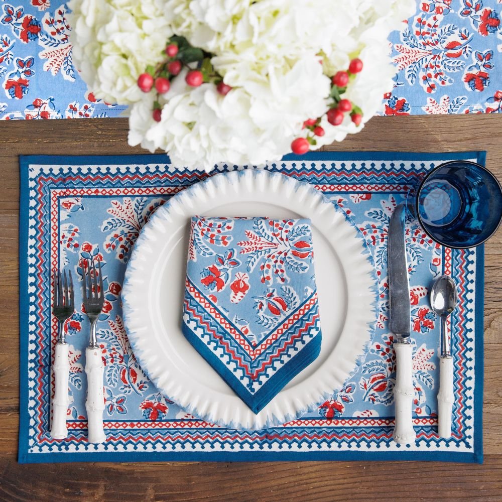 Table setting with blue and red patterned placemat, napkin, and cutlery on a wooden table.