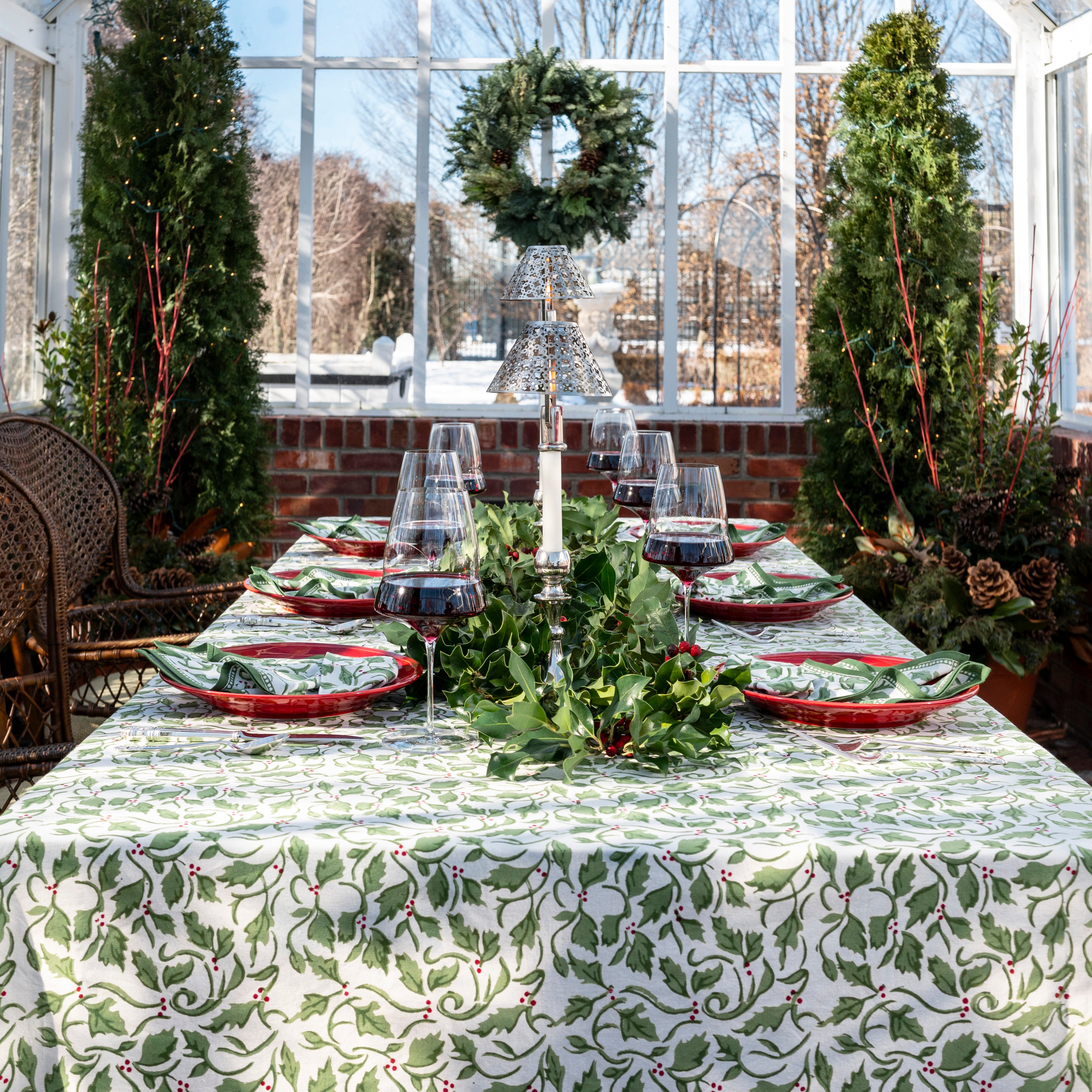 A set table covered with a green and white tablecloth featuring a holly berry pattern, arranged with dishes and silverware.