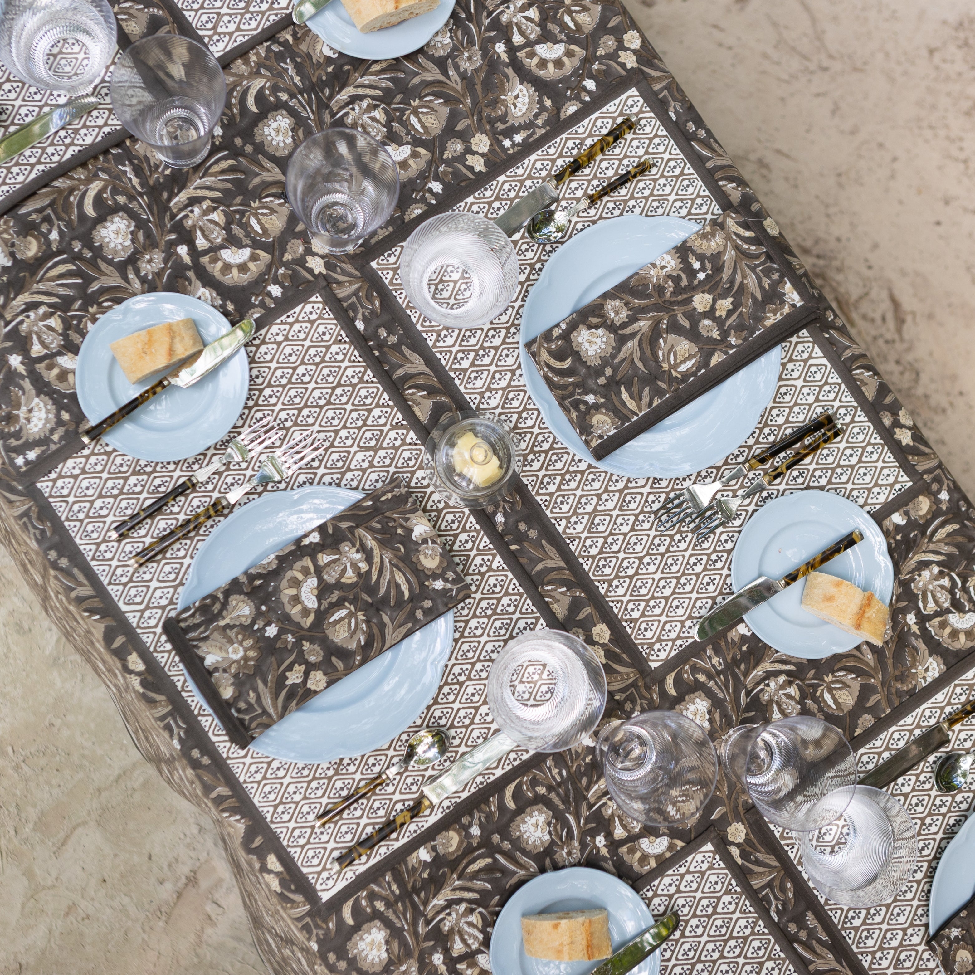 Decorative table setting with patterned tablecloth, plates, and cutlery on a textured surface.