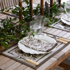 Dining table setting with greenery, plates, and cutlery on a wooden table.