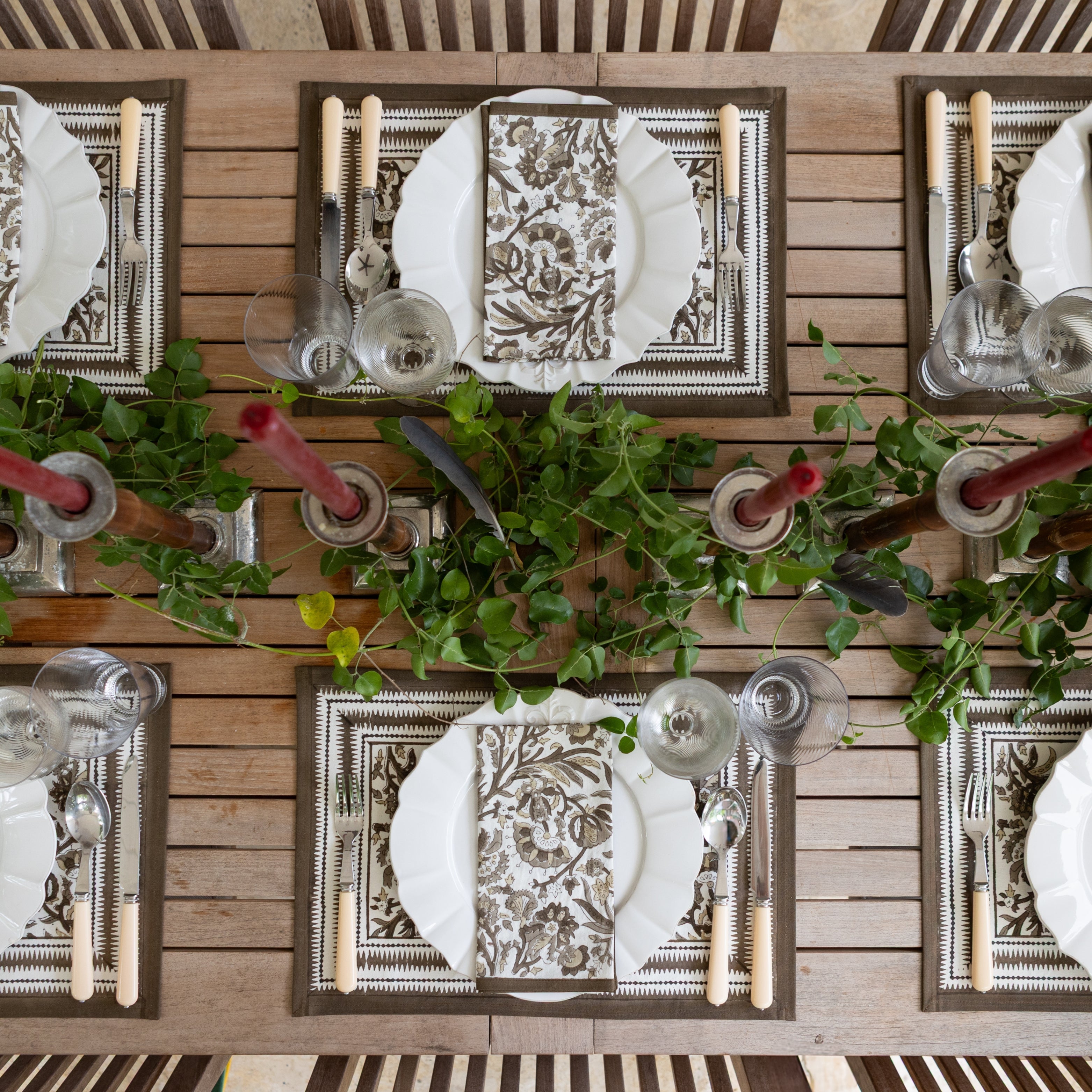 Elegant table setting with decorative plates, silverware, and candles on a wooden surface.