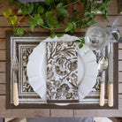 Elegant table setting with patterned placemat, white plate, and cutlery on a wooden surface.