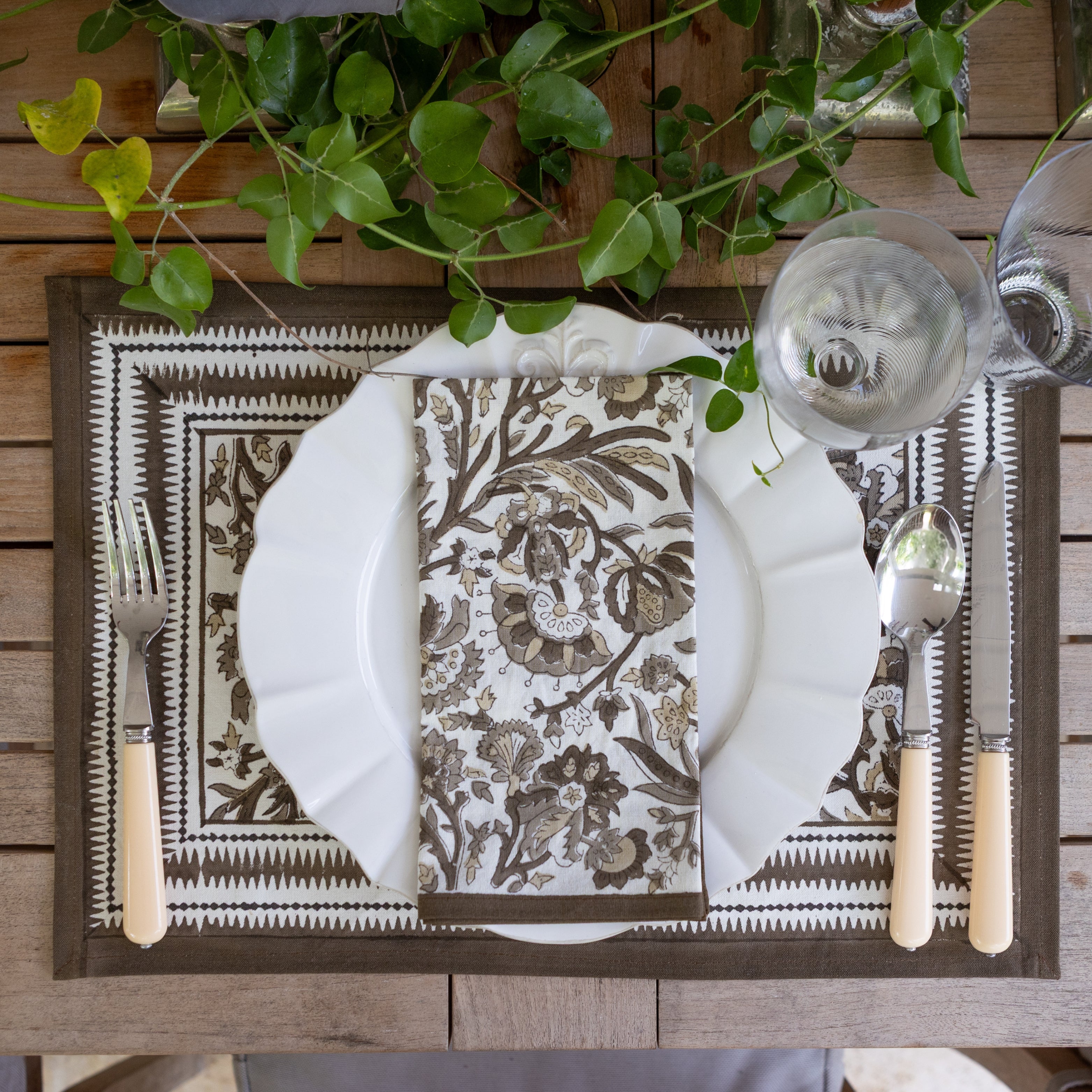 Elegant table setting with patterned placemat, white plate, and cutlery on a wooden surface.