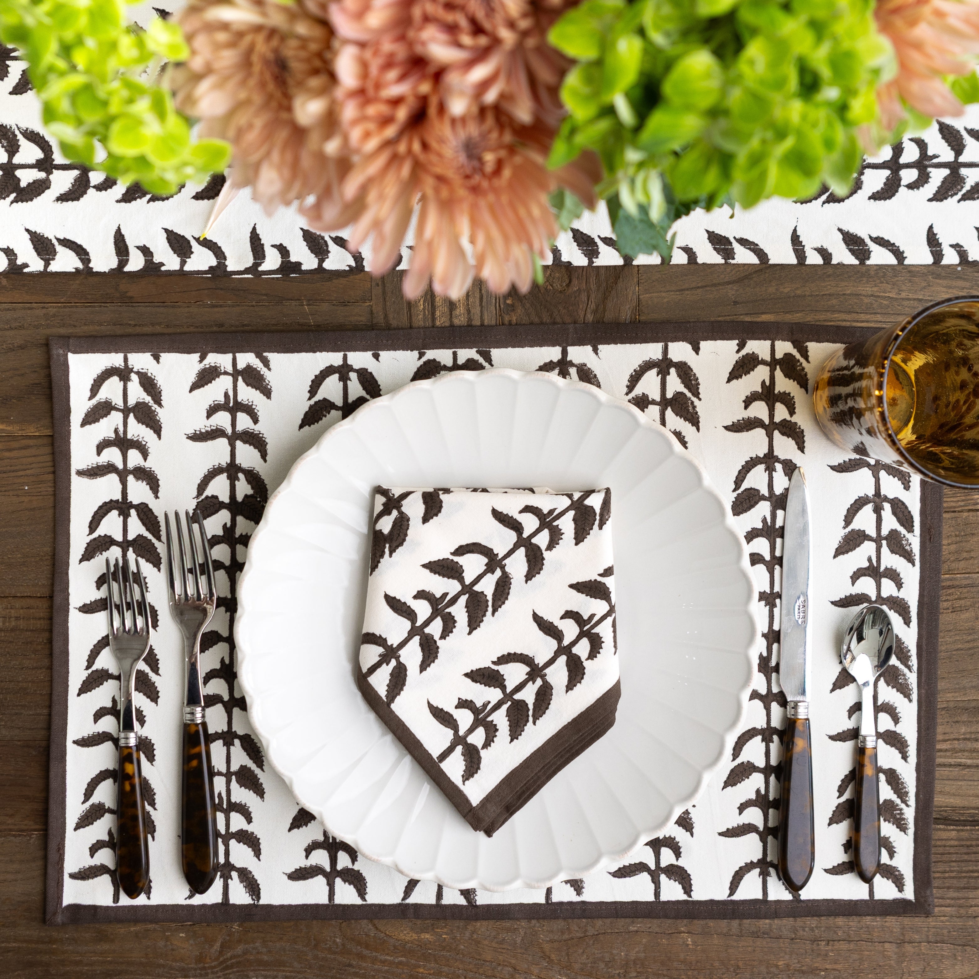 Dining table setting with white plates, cutlery, and a decorative napkin on a brown and white patterned placemat.