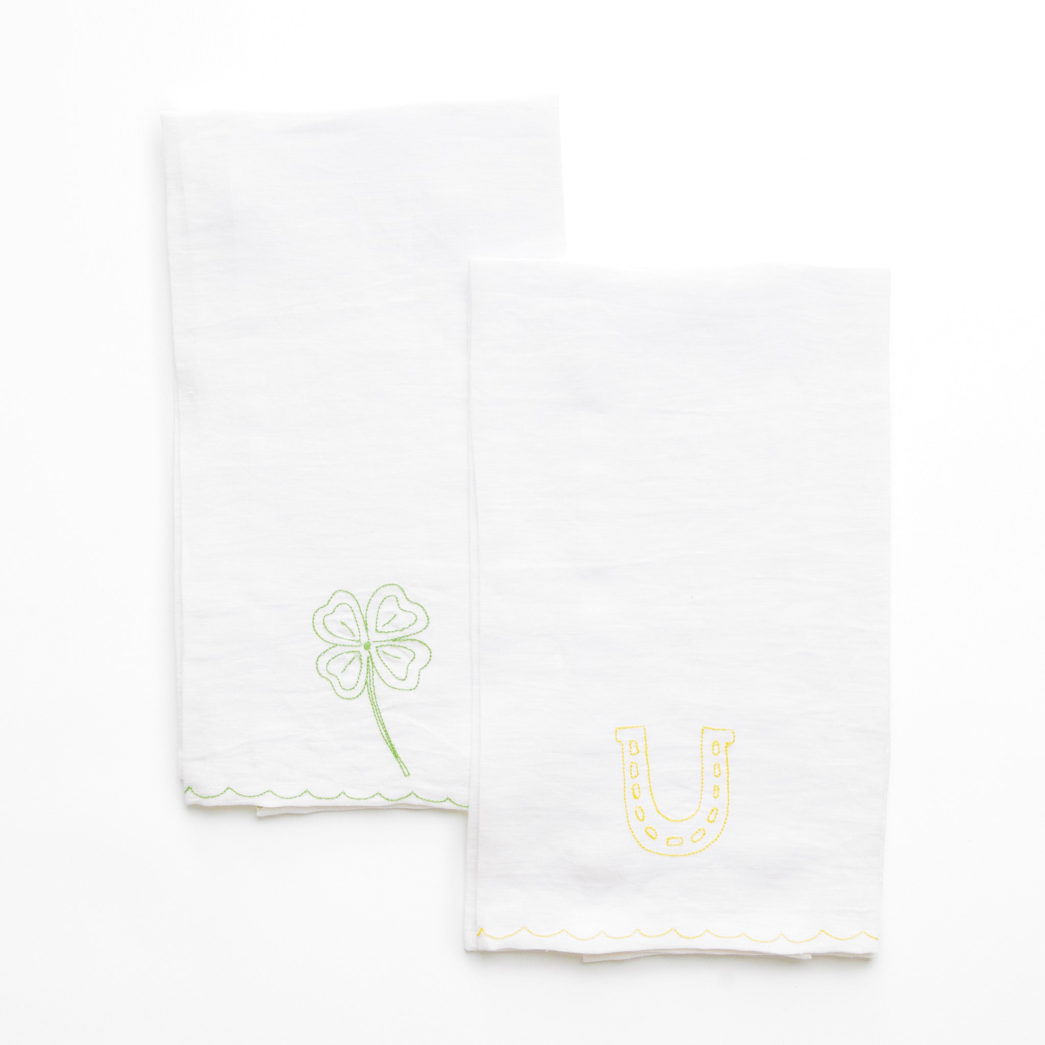 White linen kitchen tea towels embroidered with green 4 leaf clover and lucky horseshoe with scalloped border
