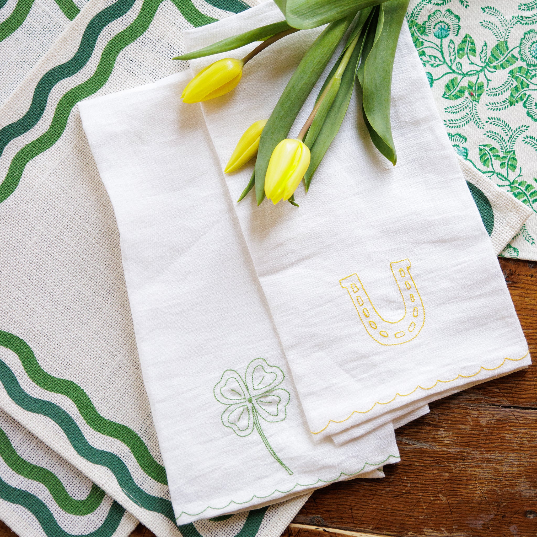 White linen kitchen tea towels embroidered with green 4 leaf clover and lucky horseshoe with scalloped border