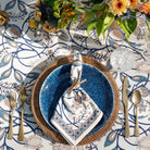 Elegant table setting with blue plates, gold cutlery, and a floral centerpiece on a patterned tablecloth.