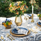 Elegant outdoor table setting with floral arrangements, gold vases, and blue plates.