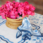Blue and white table linens with a woven basket and pink flowers. 