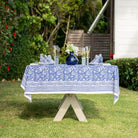 A blue and white floral patterned tablecloth is displayed on an outdoor table set for dining, with lush greenery in the background.
