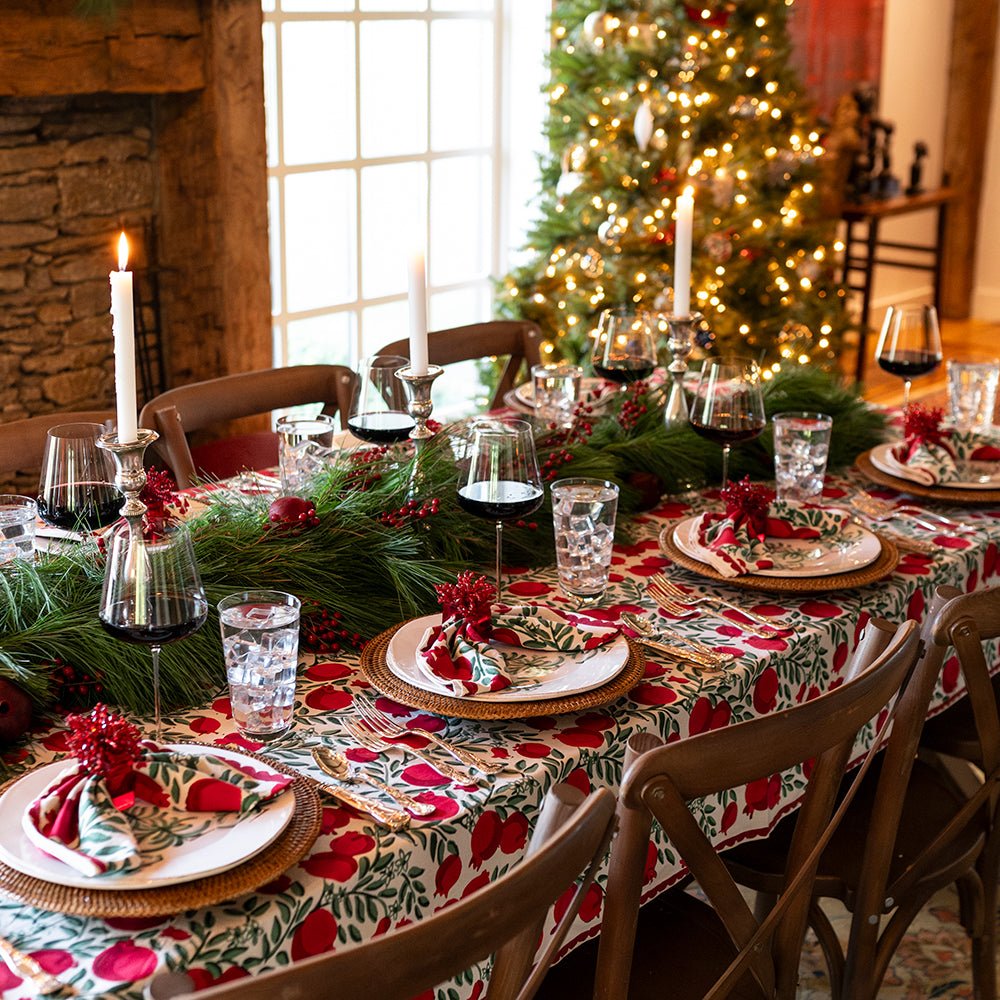 A Christmas table setting featuring pomegranate napkins and a tablecloth.