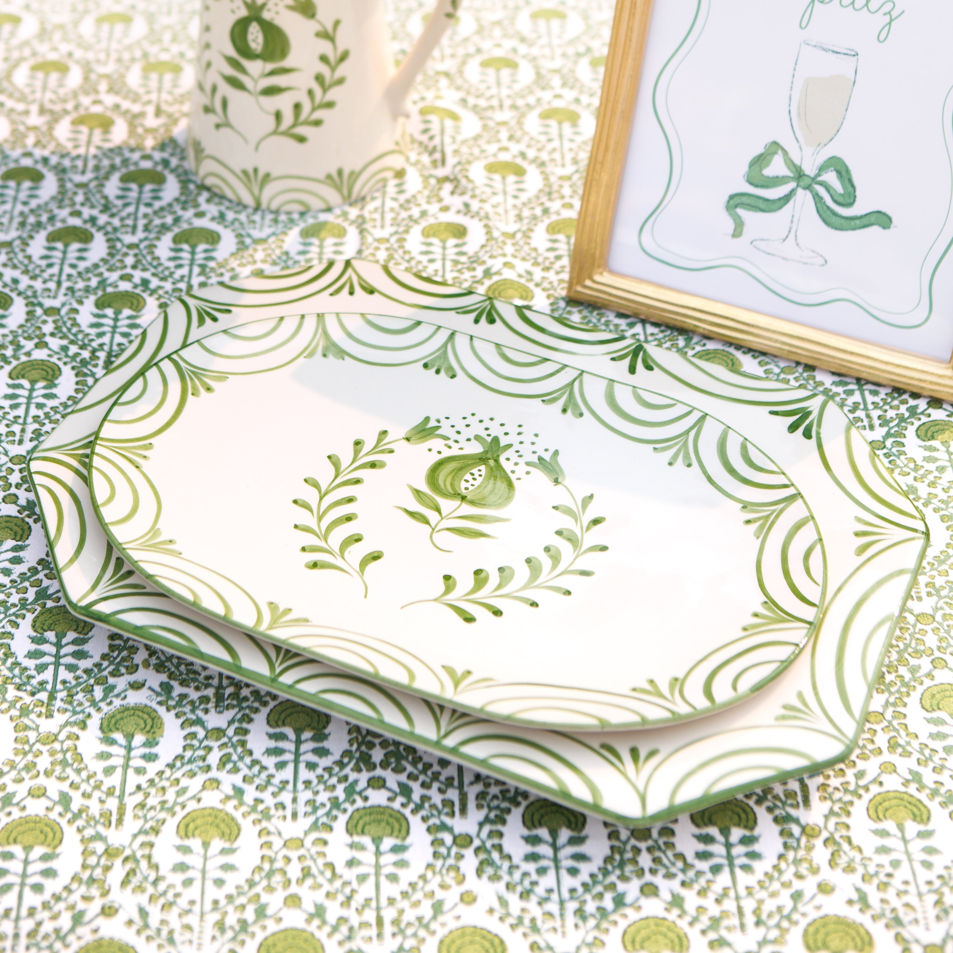 Green and white patterned platters on a matching tablecloth with a framed picture.
