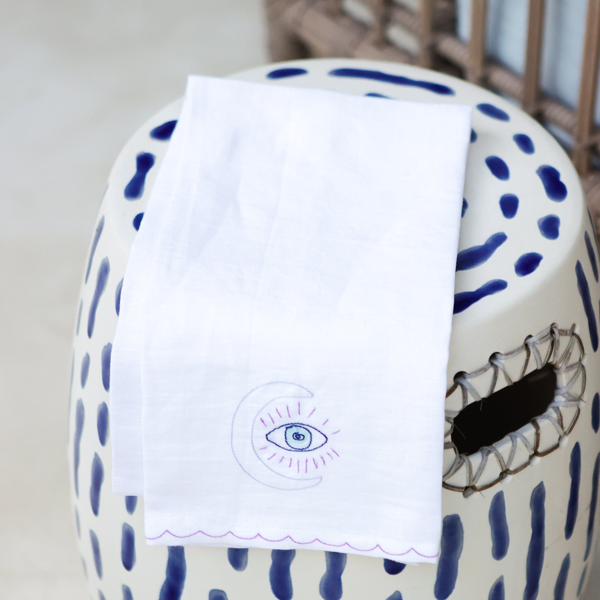 A linen tea towel with embroidered design featuring a moon with an eye symbol