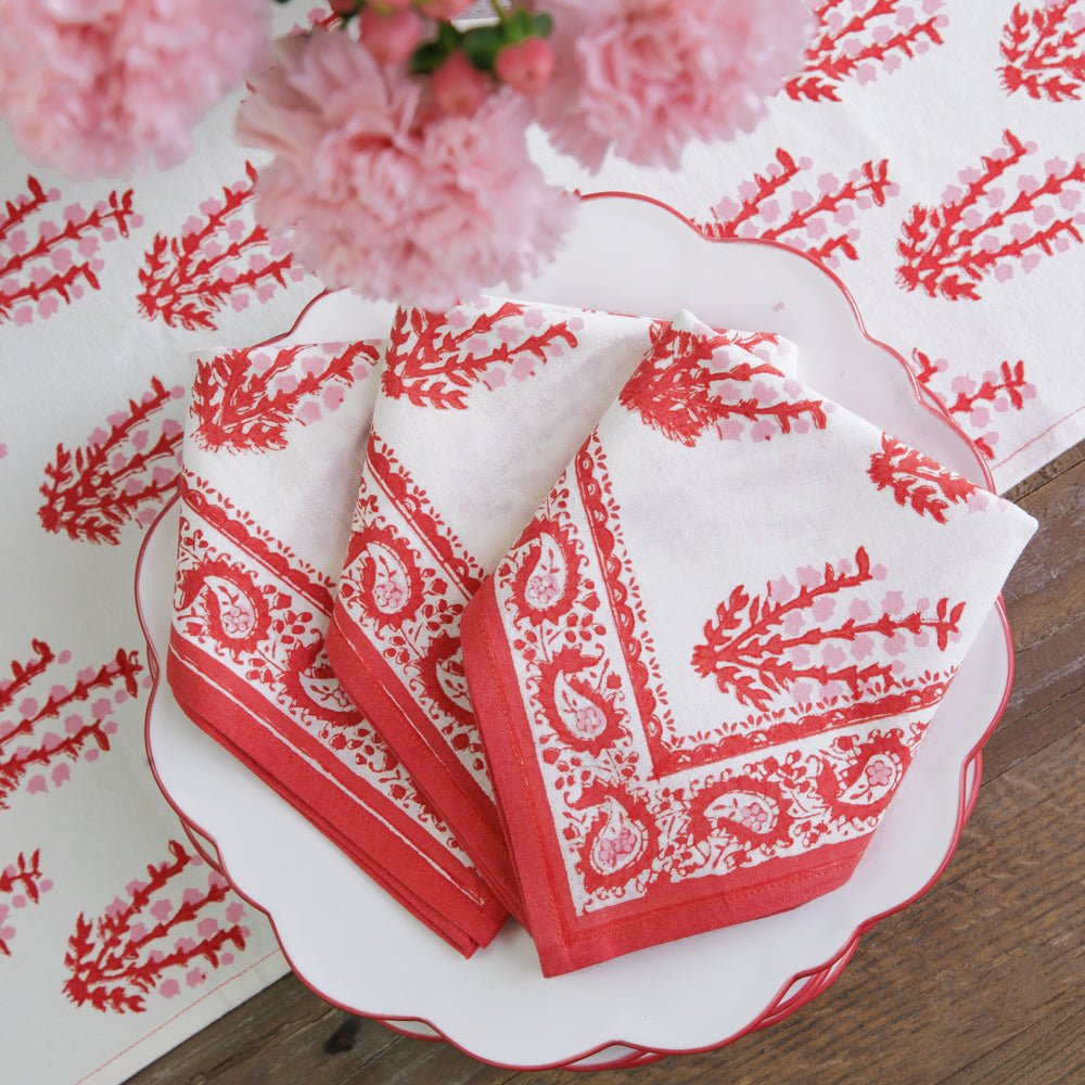 A set of folded Sagar red and white napkins with a hand block-printed design, displayed on a white plate with a floral pattern.
