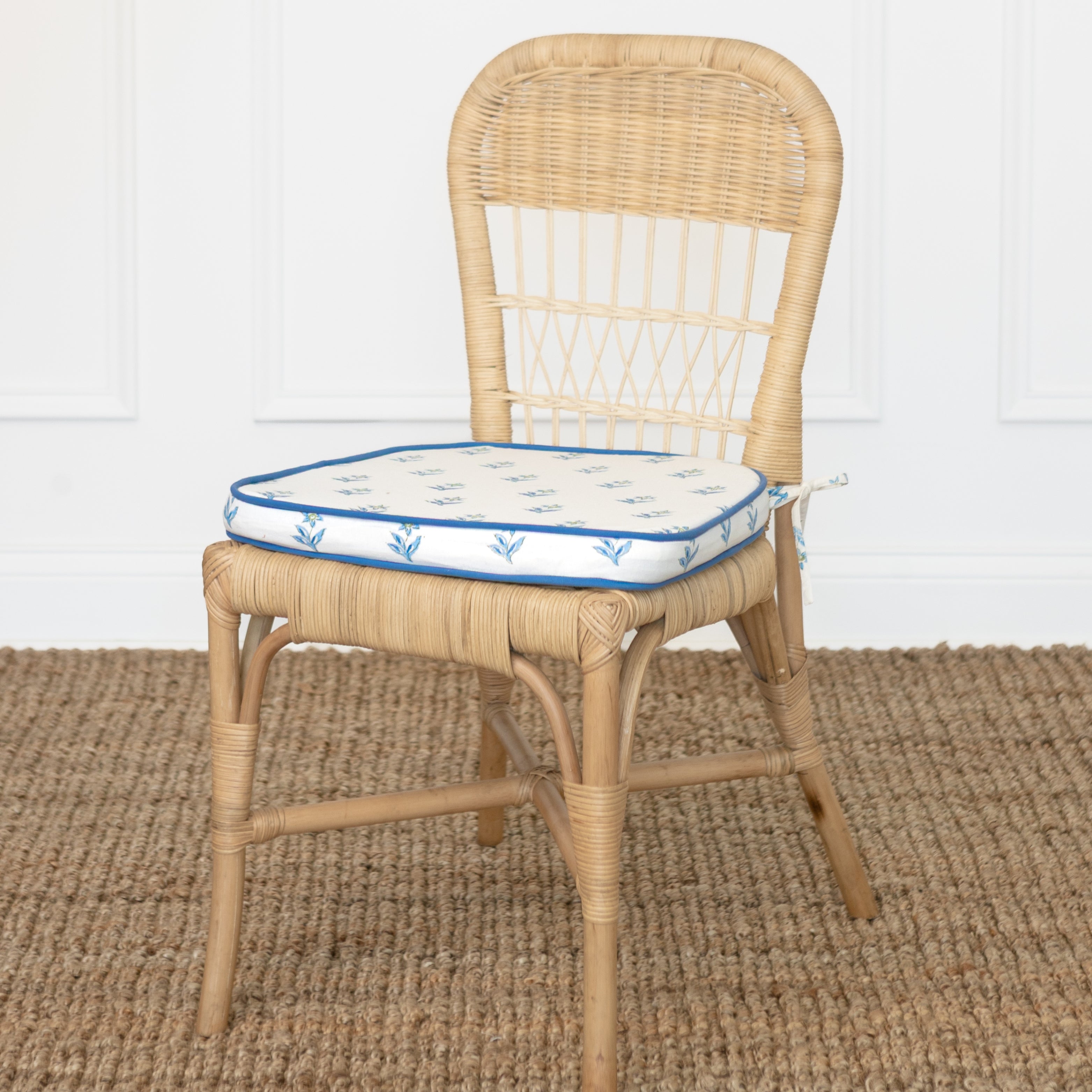 Wicker chair with a blue and white cushion on a textured brown floor.