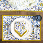 Table setting with floral placemat, plate, and cutlery on a wooden table.