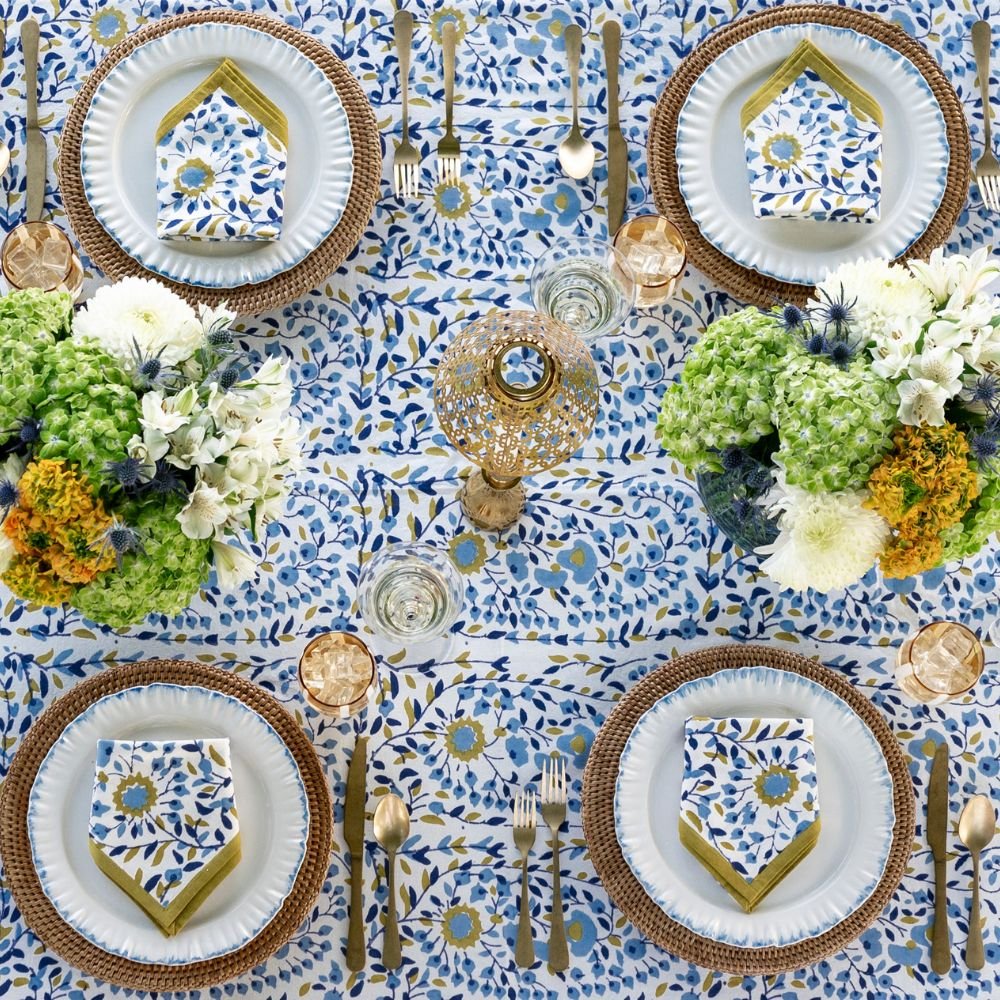 Elegant table setting with blue and white patterned tablecloth, gold cutlery, and decorative plates.