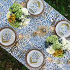Elegant outdoor table setting with floral arrangements, patterned tablecloth, and decorative plates.