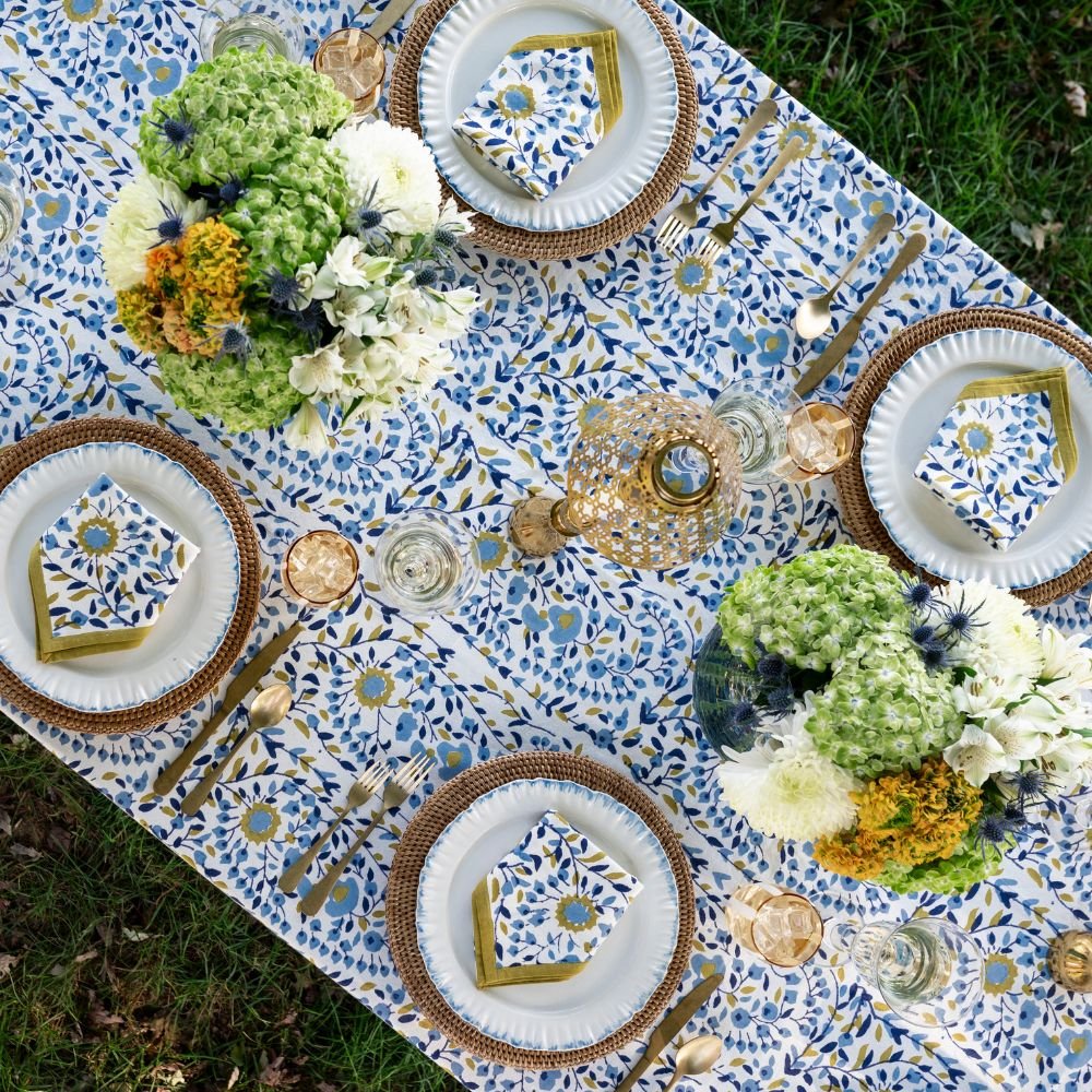 Elegant outdoor table setting with floral arrangements, patterned tablecloth, and decorative plates.