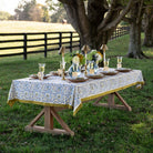 Dining table set with floral tablecloth, plates, glasses, and centerpieces outdoors.