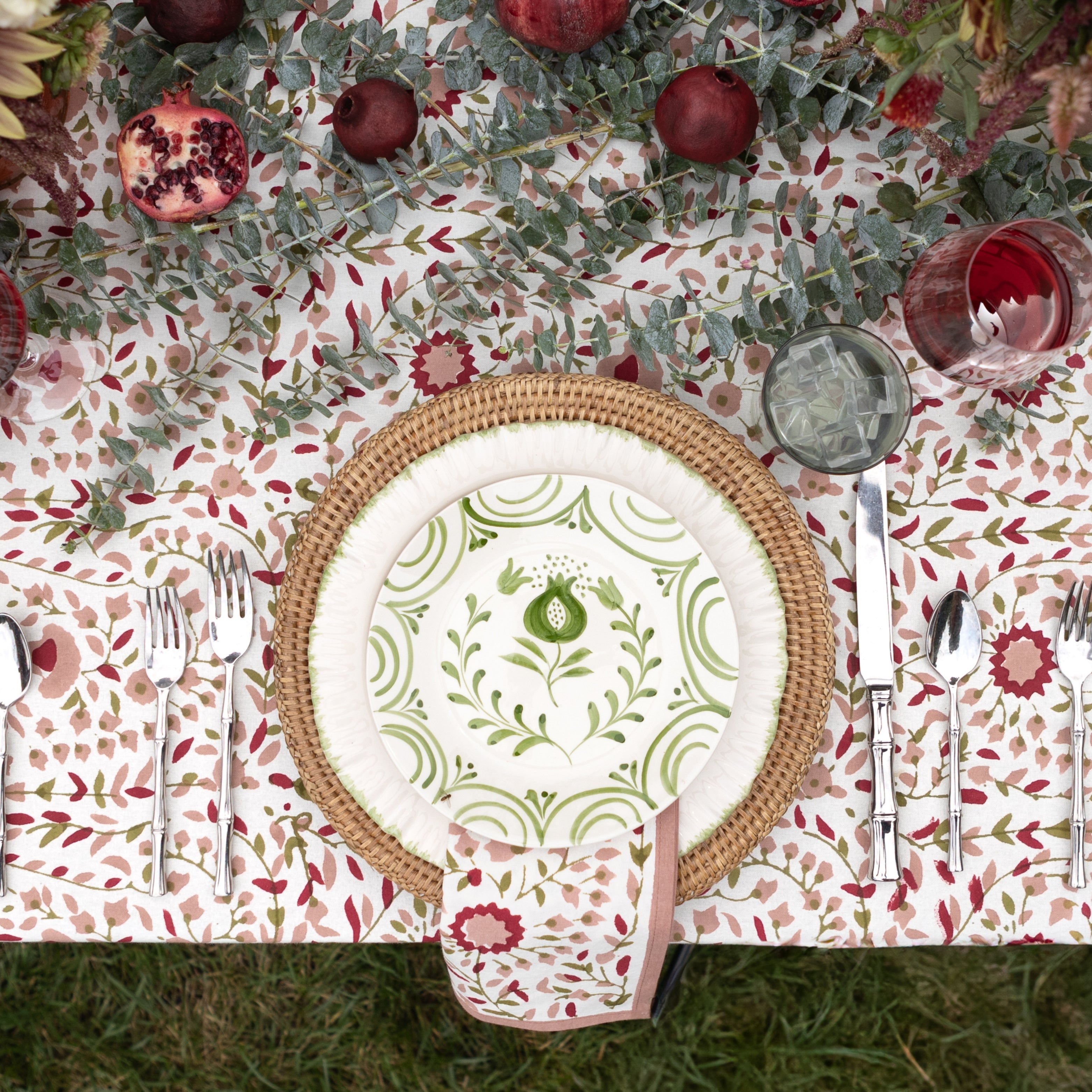Decorative table setting with floral tablecloth, woven charger, and patterned plate.
