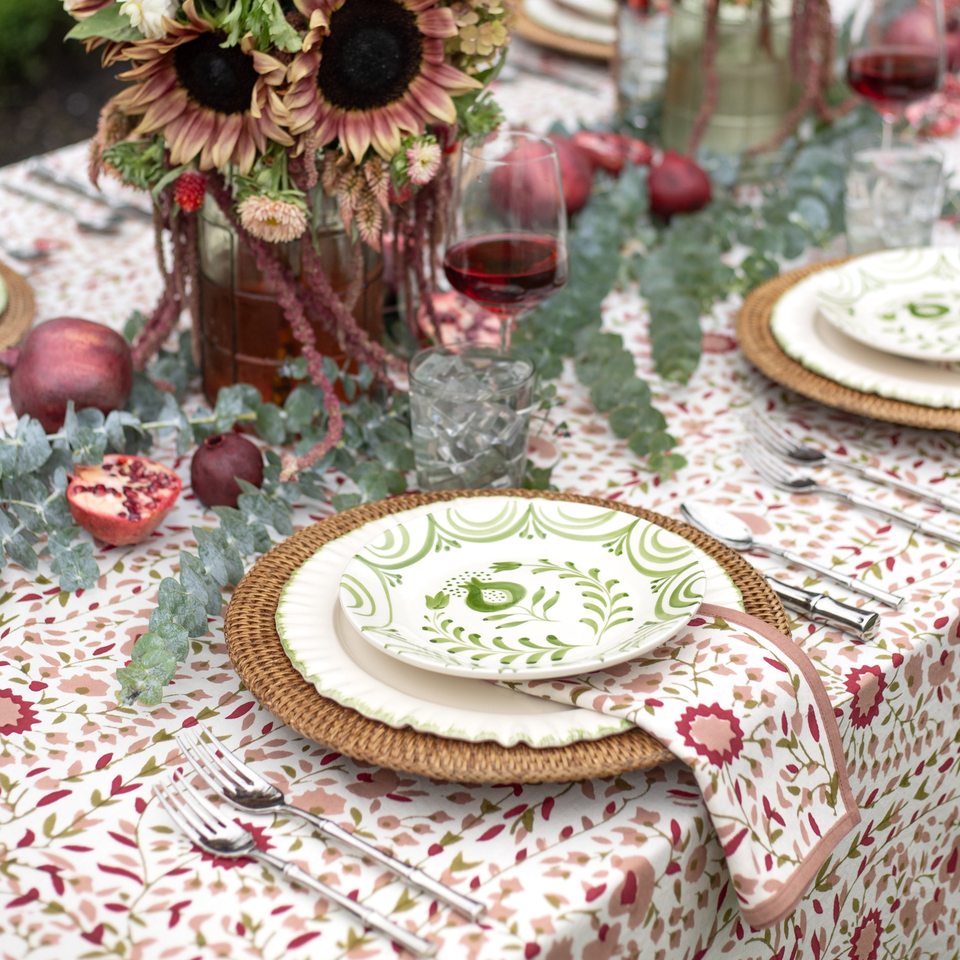 Decorative table setting with floral tablecloth, sunflowers, and pomegranates.