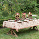 Dining table set outdoors with floral centerpieces and patterned tablecloth.