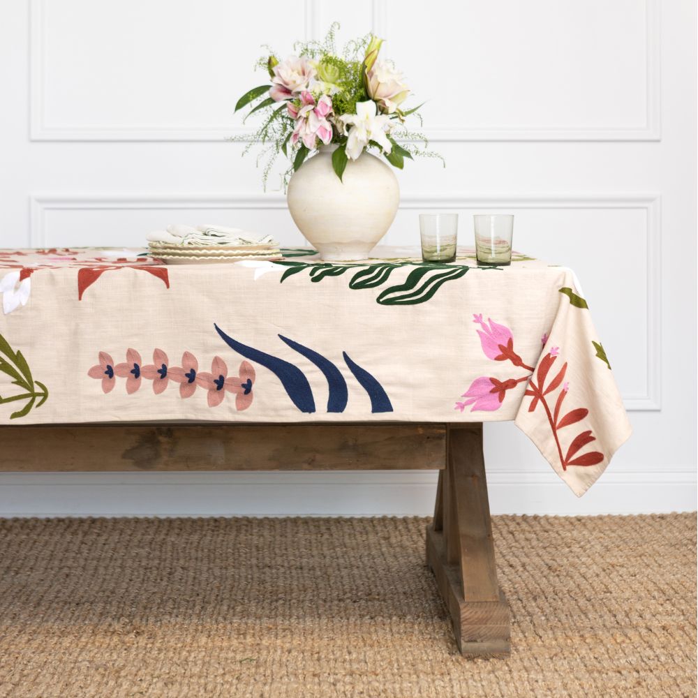 Tablecloth with floral design on a wooden table against a white wall.