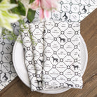 Set of folded napkins with black and white pattern on a white plate, placed on a wooden surface with a floral background.