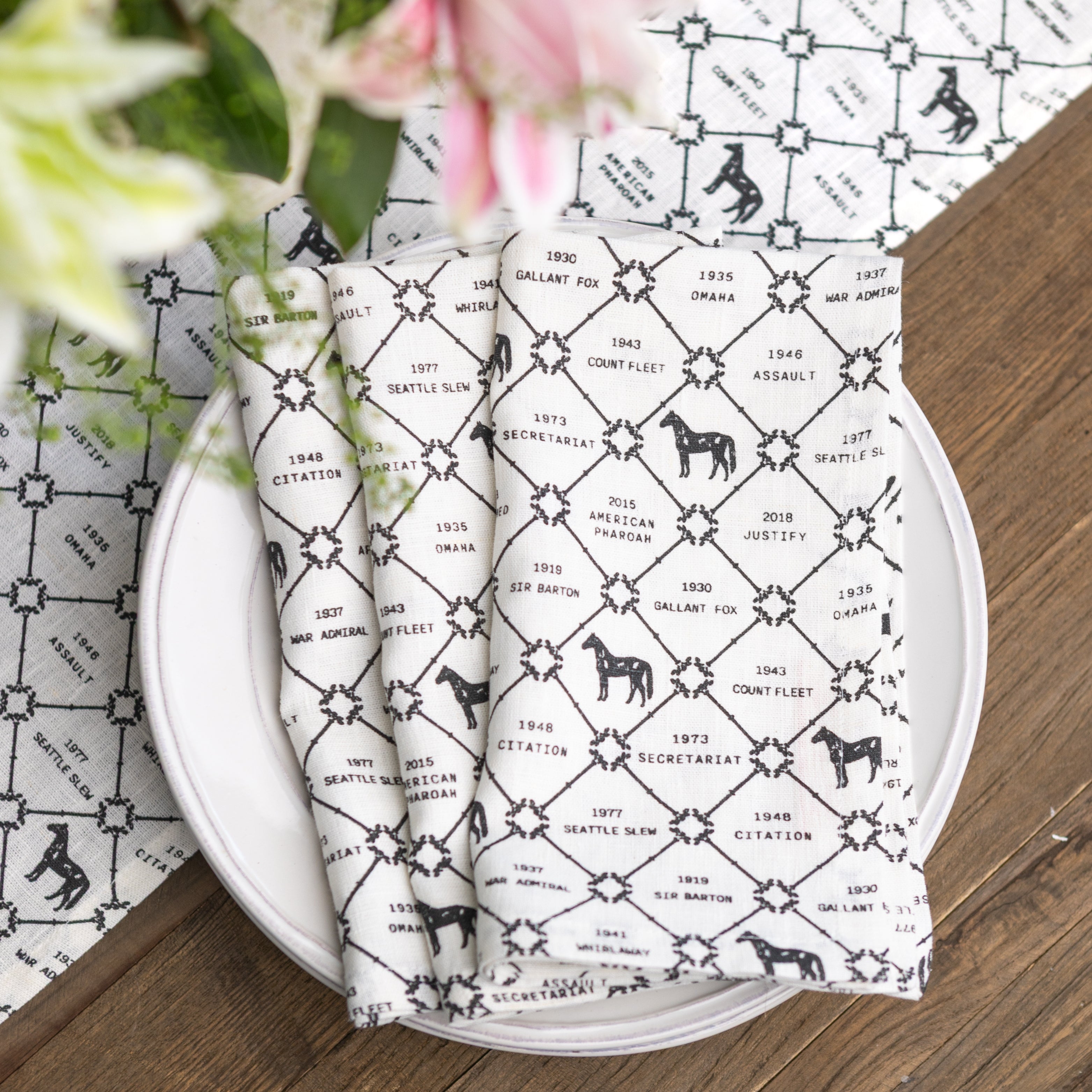 Set of folded napkins with black and white pattern on a white plate, placed on a wooden surface with a floral background.