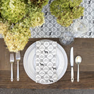 Dining table setting with white plates, silverware, and a patterned napkin on a wooden table.