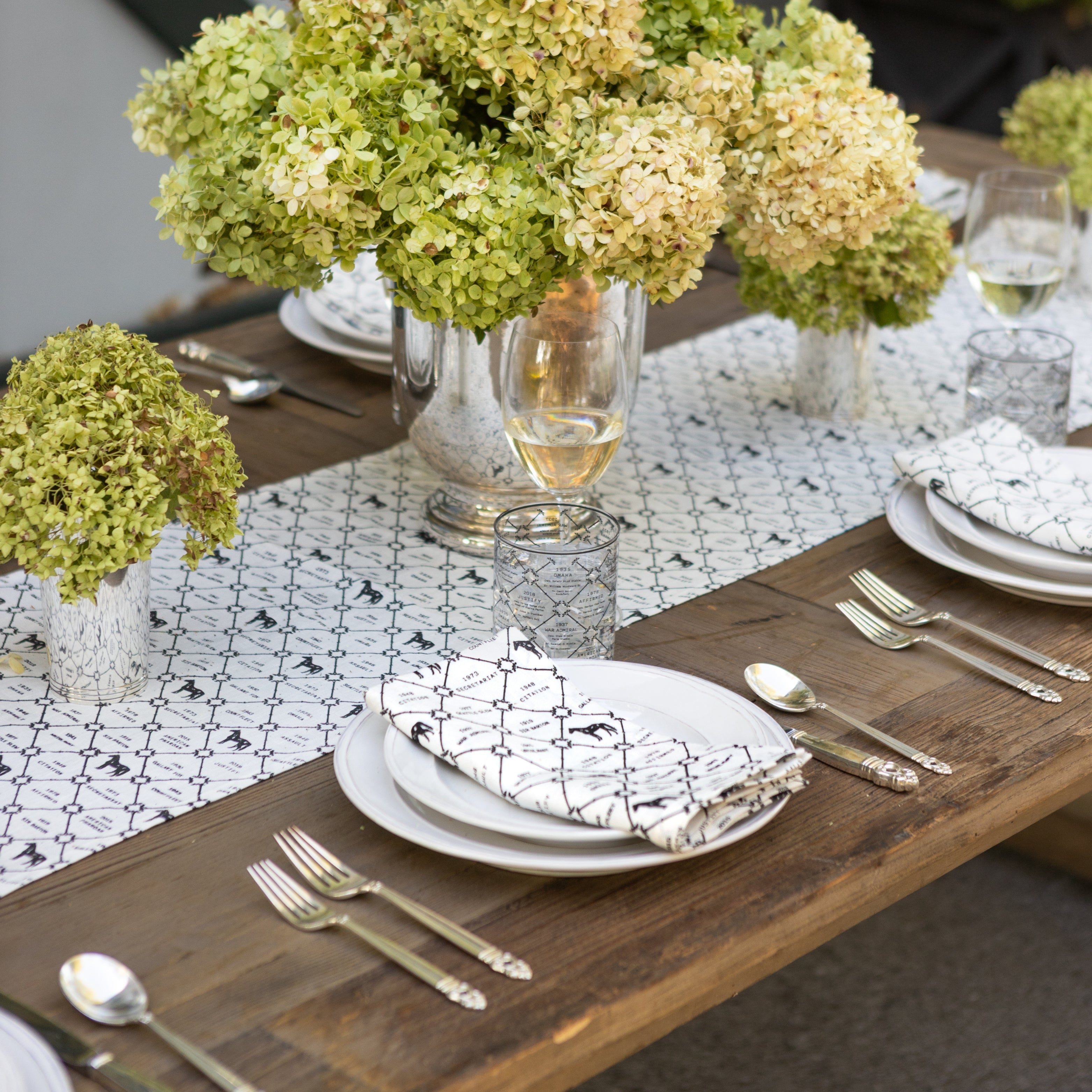 Elegant table setting with green hydrangeas, glassware, and cutlery on a wooden table.