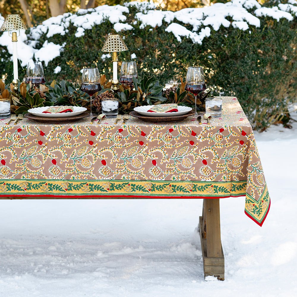 A rectangular tablecloth with a pinecone and foliage pattern, displayed on a table set for dining, with a snowy outdoor background.