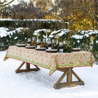 A rectangular tablecloth with a pinecone and foliage pattern, displayed on a table set for dining, with a snowy outdoor background.