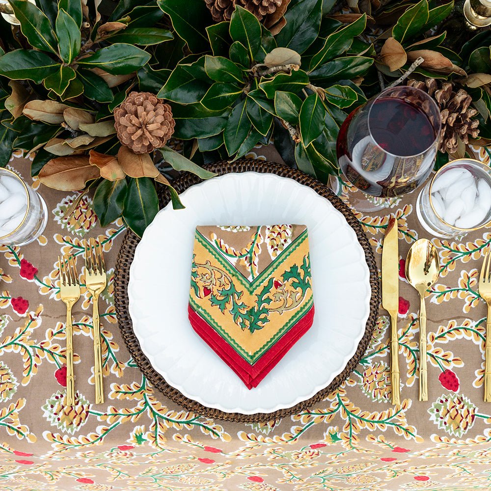 A napkin with a pinecone and foliage pattern, displayed on a table setting with cutlery and a decorative tablecloth.