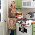 A model wearing a pinecone motif apron holding a cake in a kitchen setting