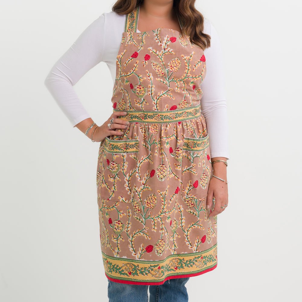 A person wearing a beige apron with a pinecone pattern, standing against a white background.