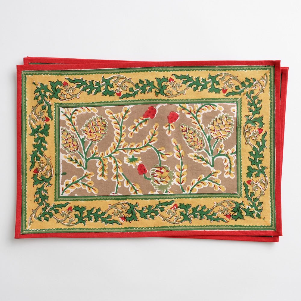 A set of four Winter Pinecone Placemats with a festive pine cone and leaf design in red, green, and gold colors on a cotton fabric.