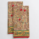 Two cotton tea towels with a hand block printed pinecone motif, greenery, and a red border.
