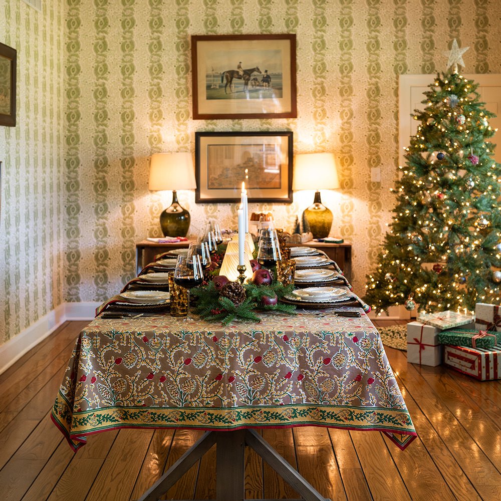 A rectangular tablecloth with a pinecone and foliage pattern, displayed on a table set for dining in doors with a Christmas tree in the background