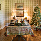 A rectangular tablecloth with a pinecone and foliage pattern, displayed on a table set for dining in doors with a Christmas tree in the background