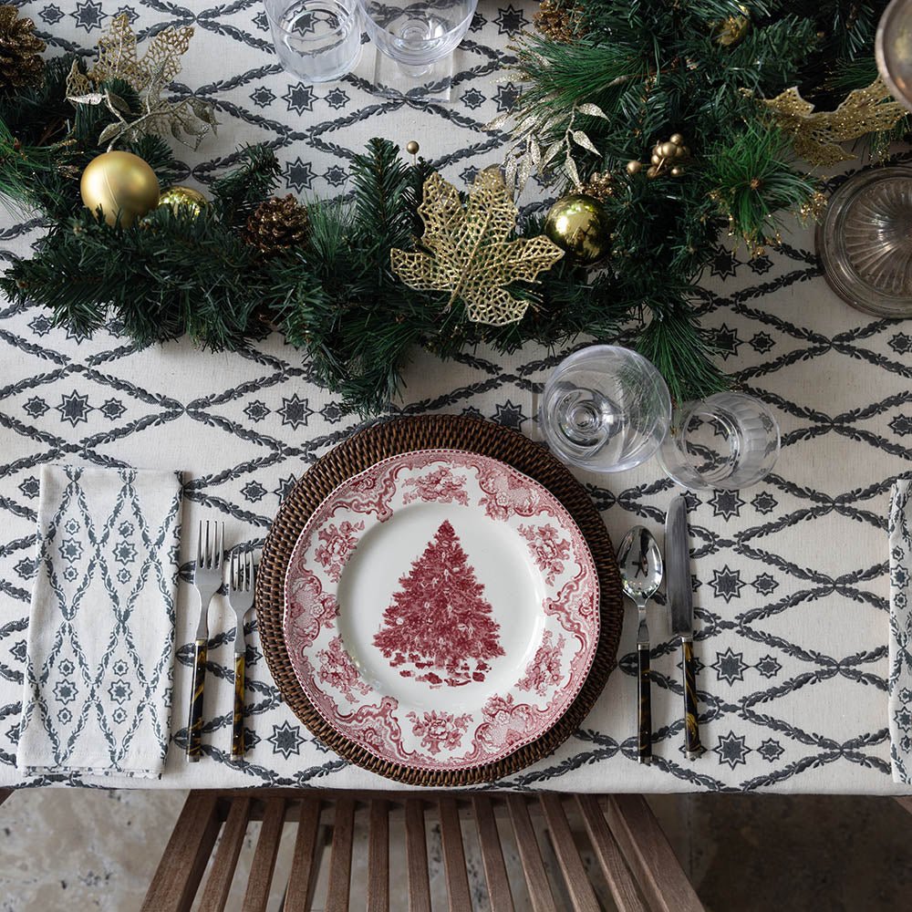A table setting featuring a geometric patterned tablecloth, arranged with plates, cutlery, and greenery.