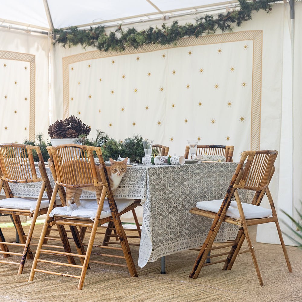 A tablecloth with a pattern resembling medals and mustaches placed on a table in a dining setting, with wooden chairs around it.