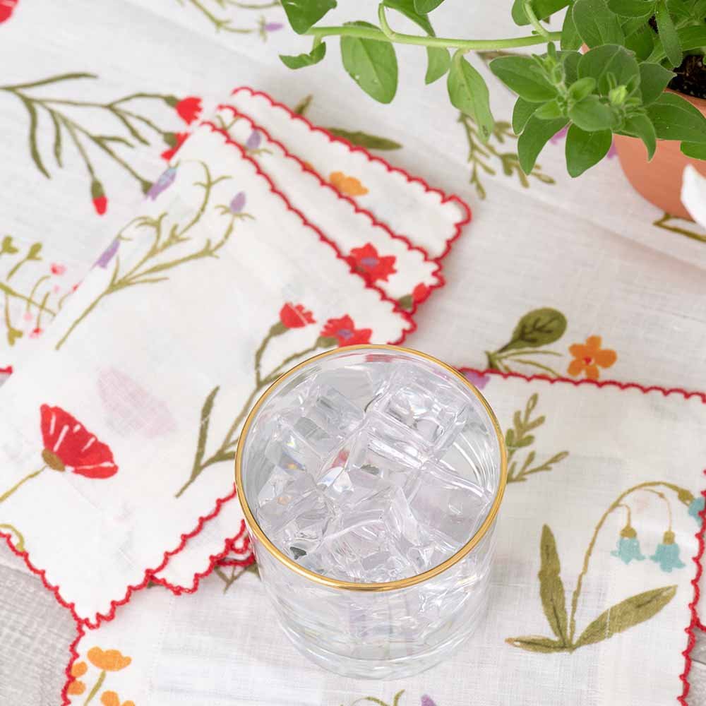 Red poppy flowers, mini yellow daffodils, and lavender bluebells on a soft white linen base.